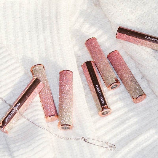 Starry lipstick collection with glittery cases in various shades on a cream fabric background.